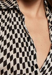 Camisa de patrón en blanco y negro con escote en V, diseño de cuello, con formas rectangulares y diamantes en un patrón alterno.