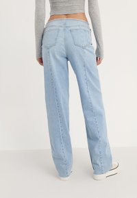 Lys blå, høy midje jeans med løs passform, synlige sømmer og fem lommer; parret med hvite sneakers med svarte detaljer.