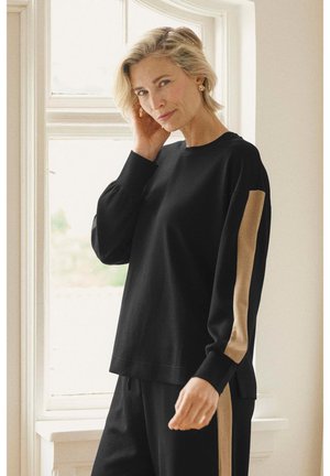 Juodas džemperis su ilgomis rankovėmis ir apvalia apykakle, puoštas smėlio spalvos akcentais ant rankovių. Minkšta medžiaga, laisvas siluetas.