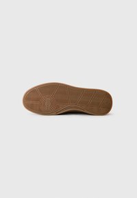 Brown rubber sole with zigzag pattern and circular logo detail. Textured finish, wide heel, and smooth edges contrasting with the tread.