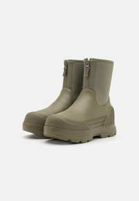 Botas de tobillo de goma verdes con un acabado liso, dos cremalleras laterales para facilitar el uso y un panel trasero texturizado para un detalle adicional.
