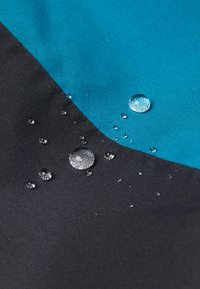 Wasserabweisender Stoff mit einem tealfarbenen und schwarzen Farbwechsel, auf dessen Oberfläche sichtbare Tropfen die Textur und Materialresistenz zeigen.