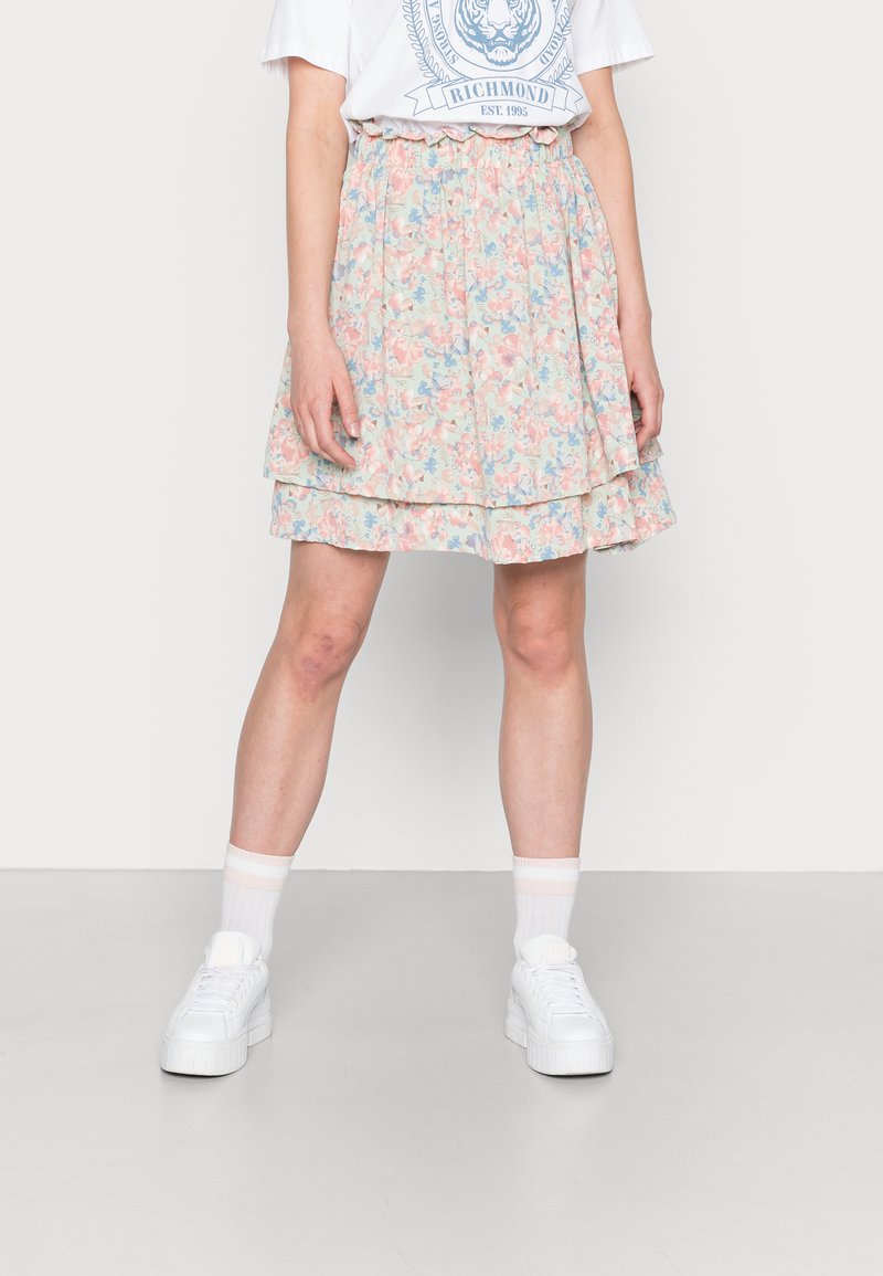 Saia floral em cores pastel com um design em camadas. Apresenta uma cintura com babados e um tecido leve. Combinada com ténis brancos e meias.