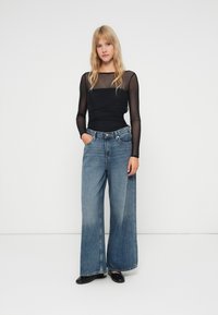 Μαύρη μακρυμάνικη μπλούζα με διαφανή υφή, συνδυασμένη με ανοιχτό μπλε παντελόνι σε φαρδιά γραμμή. Διαθέτει ψηλή μέση και κλασικό σχέδιο πέντε τσεπών.