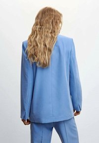 Veste légère bleu clair en tissu lisse, avec un design structuré, manches longues et coupe ajustée. Détails comprenant des coutures d'épaule nettes.
