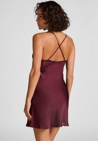 Burgunderfarbene Satin-Chemise mit Spitzenverzierungen und gekreuzten Trägern im Rücken, mit einem fließenden Saum und glatter Textur.