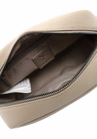 Beige Lederbeutel mit strukturierter Außenseite, Reißverschluss und glattem Innenraum. Eine kleine Tasche ist innen sichtbar, zusammen mit Etiketten.