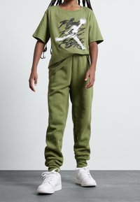 Olivgrön t-shirt i mjuk jersey med svart och vit grafik, matchad med joggingsbyxor och vita sneakers. Mjuk, avslappnad passform.