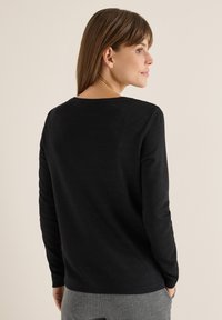 Schwarzer Langarmpullover mit Rundhalsausschnitt und weichem Material. Die Rückseite hat eine glatte Oberfläche und ist leicht tailliert.