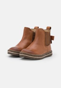 Bottines en cuir tan avec des bords festonnés, des zips latéraux et une languette à l'arrière. Dotées d'une semelle marron texturée avec des détails de couture.