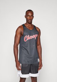 Parte superior de baloncesto de malla negra con letras rojas de "Chicago", con un corte relajado y combinada con pantalones cortos deportivos en blanco y negro.