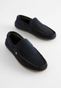 Navyblaue Wildlederloafers mit einer glatten Textur, Slip-On-Design, kontrastierenden Nähten und einem kleinen metallischen Logo-Detail an der Seite.