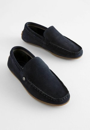 Mocassins en daim bleu marine avec une texture lisse, design à enfiler, coutures contrastées et un petit logo métallique sur le côté.