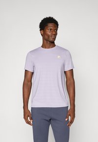 Camiseta de manga corta lila claro con sutiles rayas horizontales y un pequeño logo amarillo en el pecho, hecha de una tela suave.