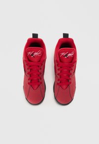 Para czerwonych sneakersów typu high-top z czarnymi podeszwami i napisem "Flight" na językach, widziane z góry na jednolitym tle.