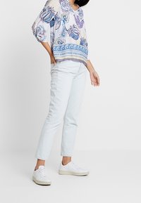 Haut léger avec un motif paisley coloré et un col en v, associé à un jean tapered bleu clair et des baskets blanches.