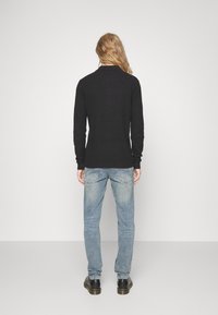 Camicia nera a maniche lunghe con texture e colletto, abbinata a jeans denim azzurri e scarpe nere, vista da dietro.
