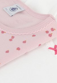 Two children's tops: one pink with small apple prints and scalloped neckline, the other white with a pink bow detail on the shoulder.