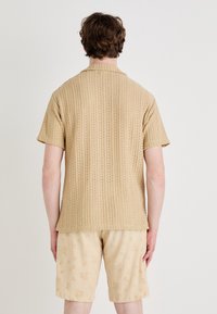 Beige geweven shirt met korte mouwen en een textuurpatroon, gecombineerd met lichtbeige shorts met een bloemenreliefdesign.