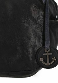 Borsa in pelle nera con finitura testurizzata. Presenta un ciondolo a forma di ancora rotonda attaccato da una tracolla blu. Chiusura con zip visibile sulla parte superiore.