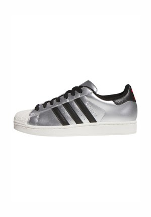 Silver synthetic sneakers with black stripes, white rubber toe cap, and black accents on the heel. Features black laces and logo detail.