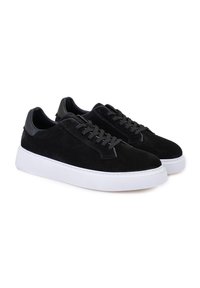 Schwarze Wildledersneaker mit einer weißen Gummisohle, runder Spitze und Schnürverschluss. Schwarze Lederdetails an der Ferse und den Ösen.