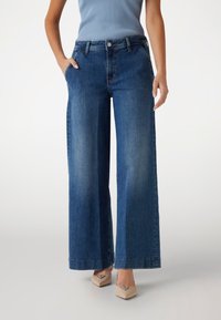 Weite Denim-Hosen in Dunkelblau mit hoher Taille, Fronttaschen und einem sauberen Abschluss am Saum. Leichte Ausbleichungen sind vorhanden.