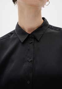 Černá košile na knoflíky s hladkým, lesklým povrchem, disponující klasickým límcem a šesti předními knoflíky.