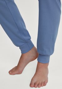 Blauwe katoenen joggers met geribbelde manchetten, gecombineerd met blote voeten. De stof heeft een gladde textuur en een relaxte pasvorm bij de enkels.