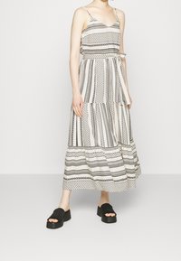 Robe maxi avec des motifs rayés noir et blanc, dotée d'un décolleté en V, de bretelles spaghetti réglables et d'un détail de taille nouée.