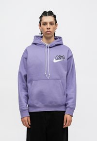 Fialová mikina s nastaviteľnými šnúrkami, prednou kapsou a bielym logom Nike. Vyrobená z mäkkej textílie, s voľným strihom a rebrovanými manžetami.