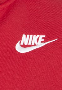 Röd tyg med en vit broderad Nike-logga. Texturen är slät med en stickad finish som betonar varumärkets signaturdesign.