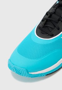 Scarpa sportiva turchese realizzata in materiali mesh e sintetici. Presenta un design con lacci neri e una suola testurizzata con motivi di trazione.