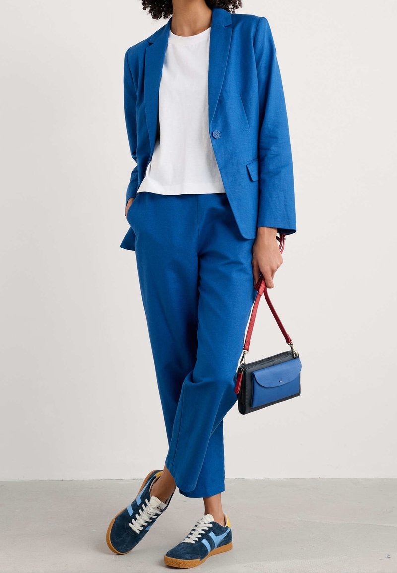 Blå skräddarsydd blazer och matchande byxor, vit t-shirt under, kombinerat med blå och vita sneakers, samt en liten blå handväska med röd rem.