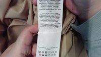 Tela de poliéster beige con una textura suave, sostenida con una etiqueta de cuidado que muestra múltiples idiomas e instrucciones de cuidado.