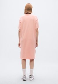 Ροζ βαμβακερό φόρεμα σε πολύ μεγάλο μέγεθος με κοντά μανίκια, που φτάνει λίγο πάνω από το γόνατο, με πλευρικές σχισμές, σετ με λευκές κάλτσες και αθλητικά παπούτσια με σχέδια.