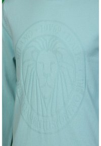 Sweater bleu clair avec un logo de lion embossé dans le tissu, au toucher doux et avec un col rond.