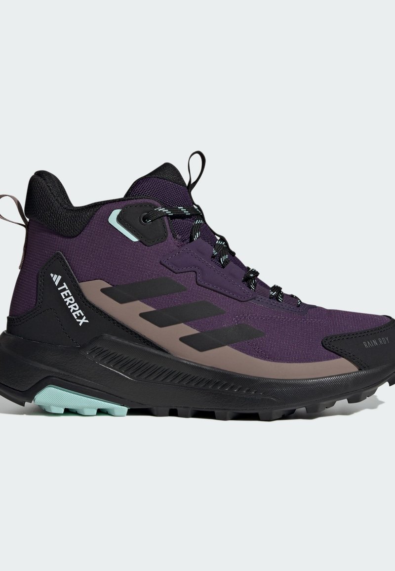 Bota de senderismo púrpura con acentos en negro y gris, parte superior texturizada, talón reforzado y suela de goma. Presenta cordones con patrón y detalle del logo.