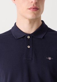 Navyblå pikétröja i texturerad tyg, med en klassisk krage, två knappar fram och en liten broderad logotyp.