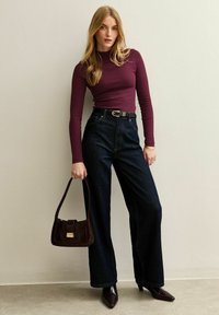 Vinsvart långärmad topp, hög midja mörka denim vida byxor, svart bälte och brun texturerad handväska, tillsammans med spetsiga klackar.