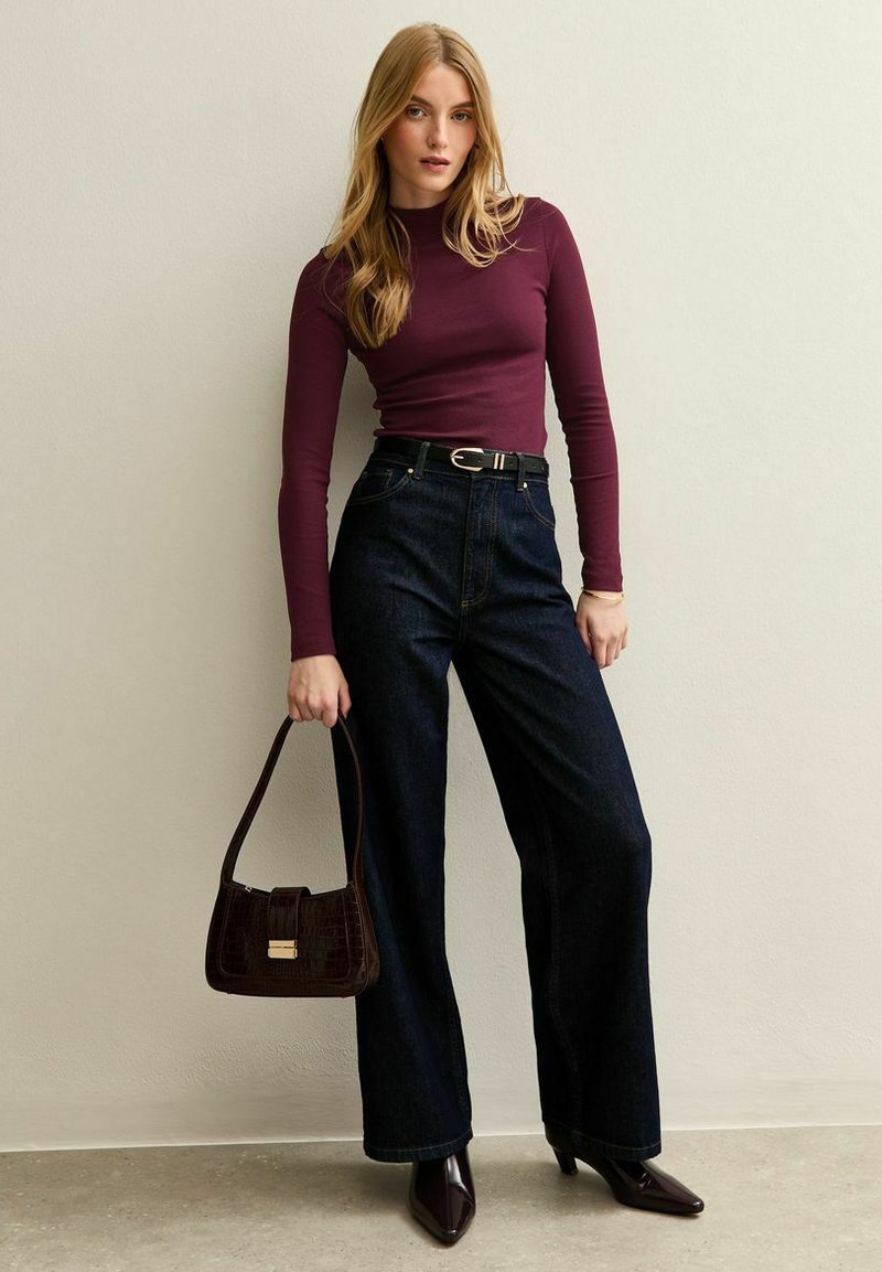 Vinsvart långärmad topp, hög midja mörka denim vida byxor, svart bälte och brun texturerad handväska, tillsammans med spetsiga klackar.