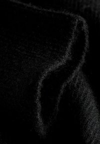 Zbliżenie miękkiej, czarnej tkaniny wełnianej z widocznymi drobnymi włóknami i teksturowanymi fałdami, które tworzą cienie i głębię na ciemnym tle.