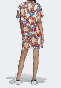 Korte mouwen jurk met een witte basis, voorzien van een kleurrijk bloemen- en ornamentenpatroon in rood, blauw en bruin, gecombineerd met zwart-witte sneakers.