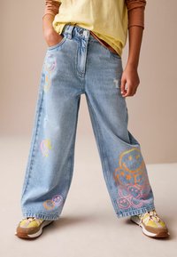Lyseblå jeans med vide ben, farverige smily- og hjerte-motiver, slidte detaljer og fem-lomme-design.