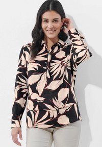 Langärmlige Bluse mit schwarzem Hintergrund und großen, hellrosafarbenen und roten Blumenmustern, mit kragenförmigem Ausschnitt und Knopfschluss.