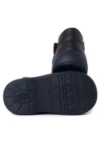 Zapatos de cuero negro con una suela de goma texturizada, que presentan una superficie lisa, punta redondeada y una correa de velcro para el cierre.