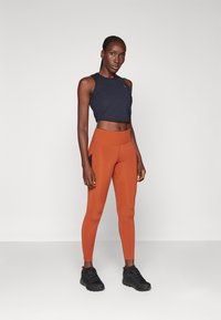 Navy cropped urheilutoppi yhdistettynä ruosteenvärisiin korkeavyötäröisiin legginsseihin, joissa on sivutaskut. Mustat urheilukengät viimeistelevät asun.