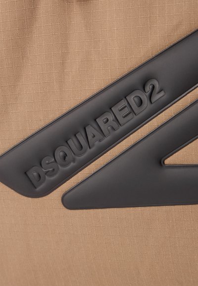 Tansinine kangas, millel on tekstuuriga muster, sisaldab musta kummi logo "DSQUARED2", millele on lisatud kontrastne must geomeetriline disainielement.