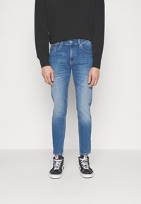 Blå denimjeans med en smal passform, blekta detaljer på låren och en klassisk femfickdesign, bärs med svarta högre sneakers.