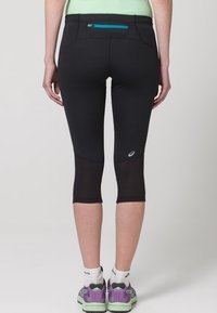 Černé sportovní legíny s kapsou na zip, síťovanými panely a přiléhavým střihem, kratšími do půli lýtek. Výrazné logo na boku.